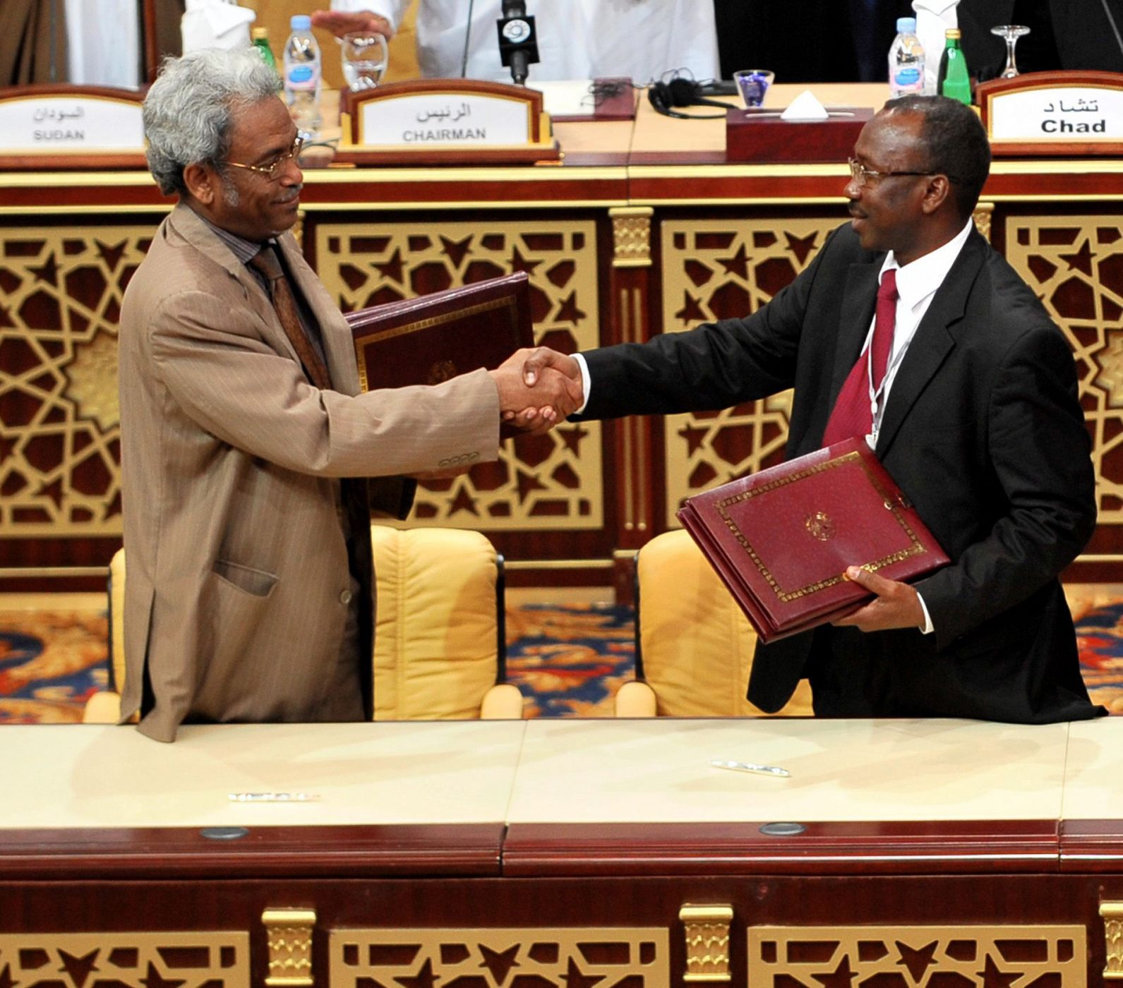 El representante del Gobierno de Sudán, Omar Amin Hassan Omar (izquierda) y el del JEM, Ahmed Tugod Lsan, se dan la mano tras firmar el acuerdo de paz en el hotel Sheraton de Doha.