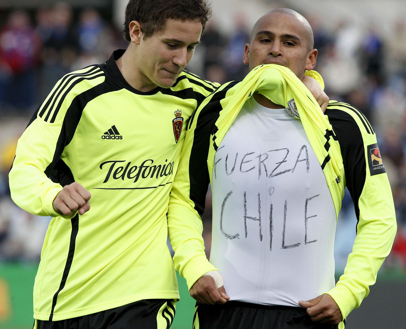 El delantero chileno del Real Zaragoza Humberto 'Chupete' Suazo (d) muestra, junto a su compañero Ander Herrera, una camiseta en solidaridad con su país