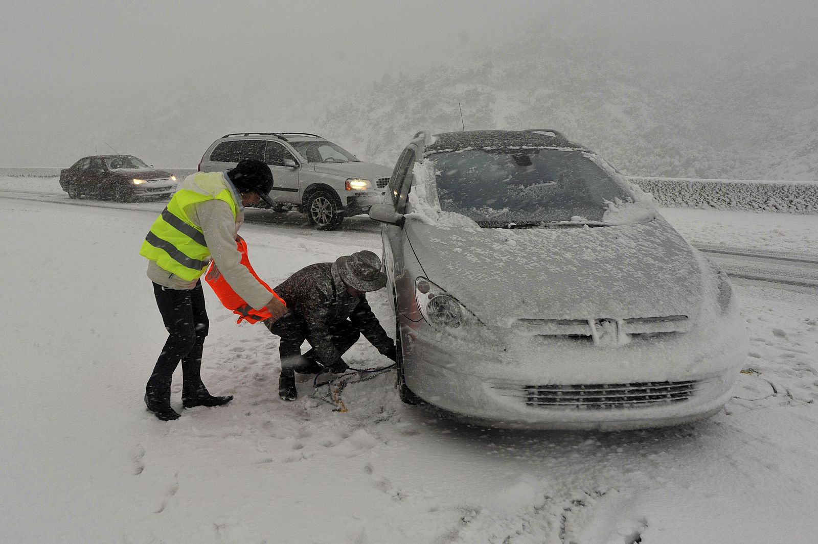 Dos automovilistas colocan cadenas en sus coches en el paso fronterizo de la Jonquera, cerrado al tráfico a todo tipo de vehículos debido al temporal de nieve.