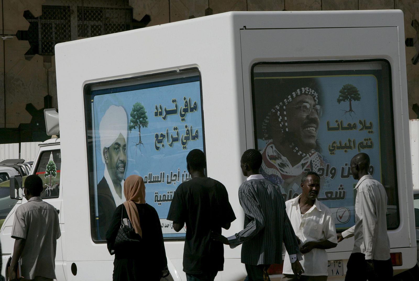 Un grupo de personas camina junto a unos carteles donde aparese el presidente sudanés Omar al-Bashir