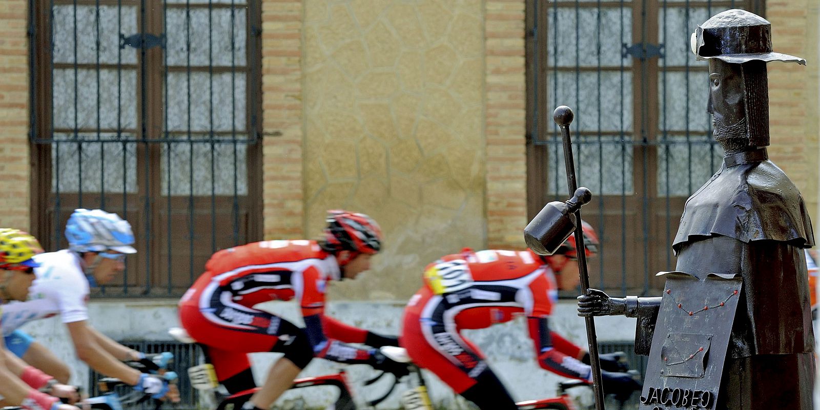 Los corredores de la Vuelta a Castilla y León pasan delante de una estatua del peregrino.