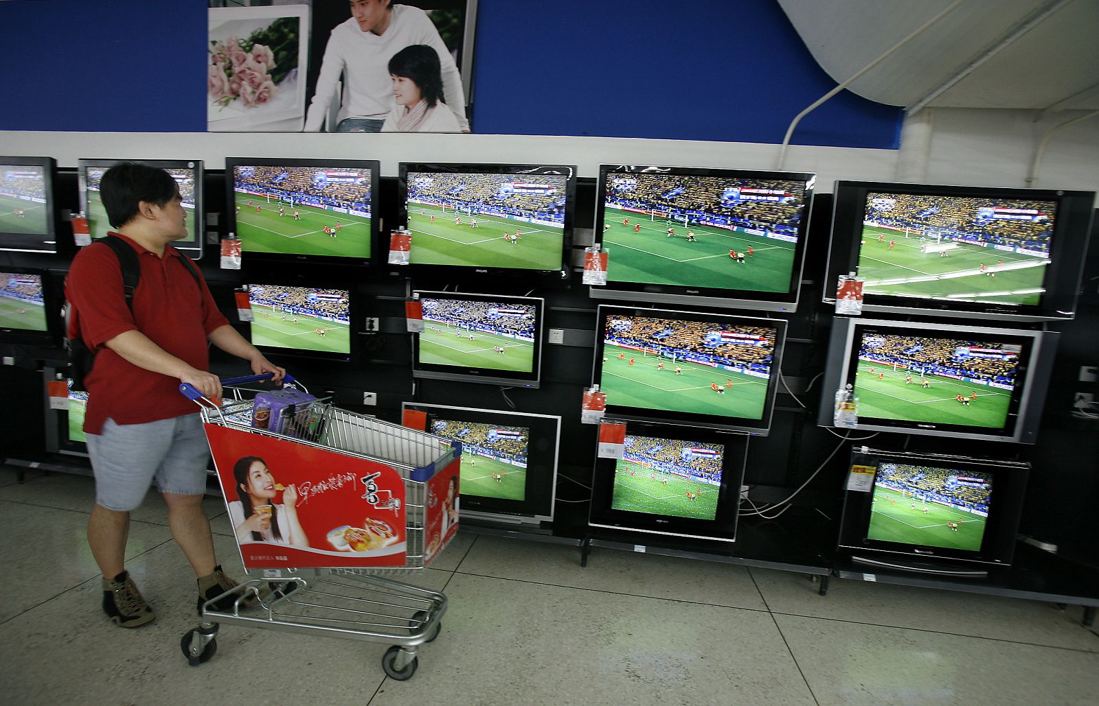 Un cliente chino observa los televisores de una tienda emitiendo imágenes de fútbol.