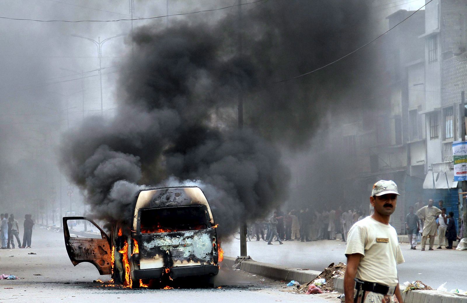 Una columna de humo emerge de los restos de un vehículo calcinado por las calles de Karachi tras los disturbios por el asesinato de un diputado provincial.