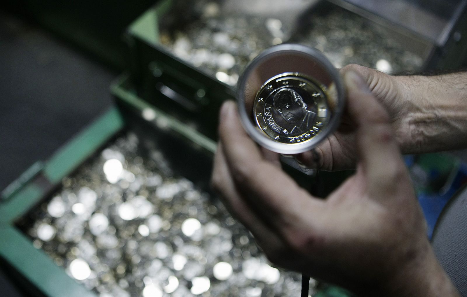 A mint worker displays a 1 euro coin mould depicting Spanish King Juan Carlos with a magnifying glass in Madrid