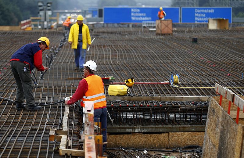 Construction workers are seen in front of highway signs as they work on a taxiway bridge for airplanes over highway A3 at airport extension in Frankfurt