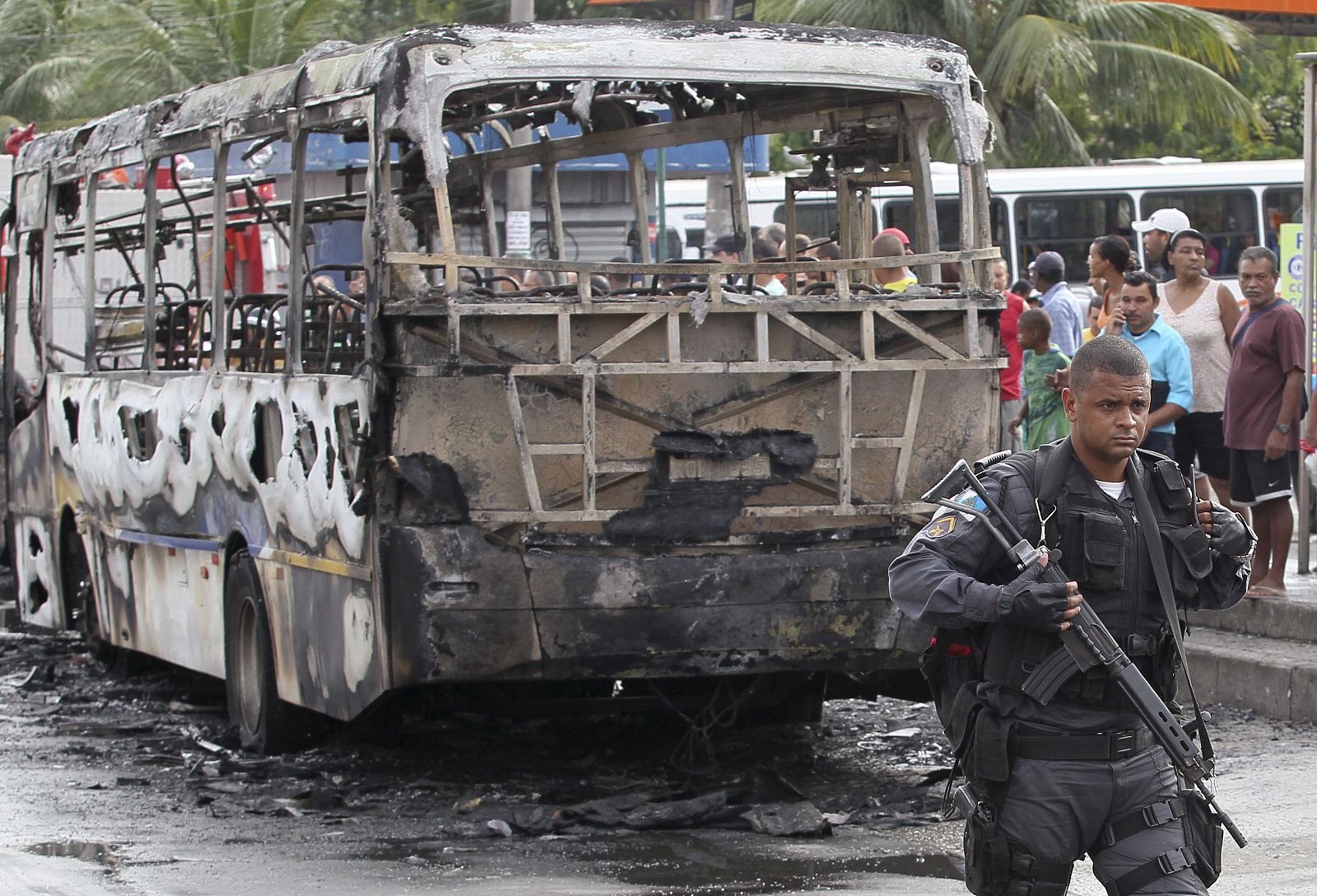 Un policíía brasileño, junto  a un autobús quemado por los narcos en Río.