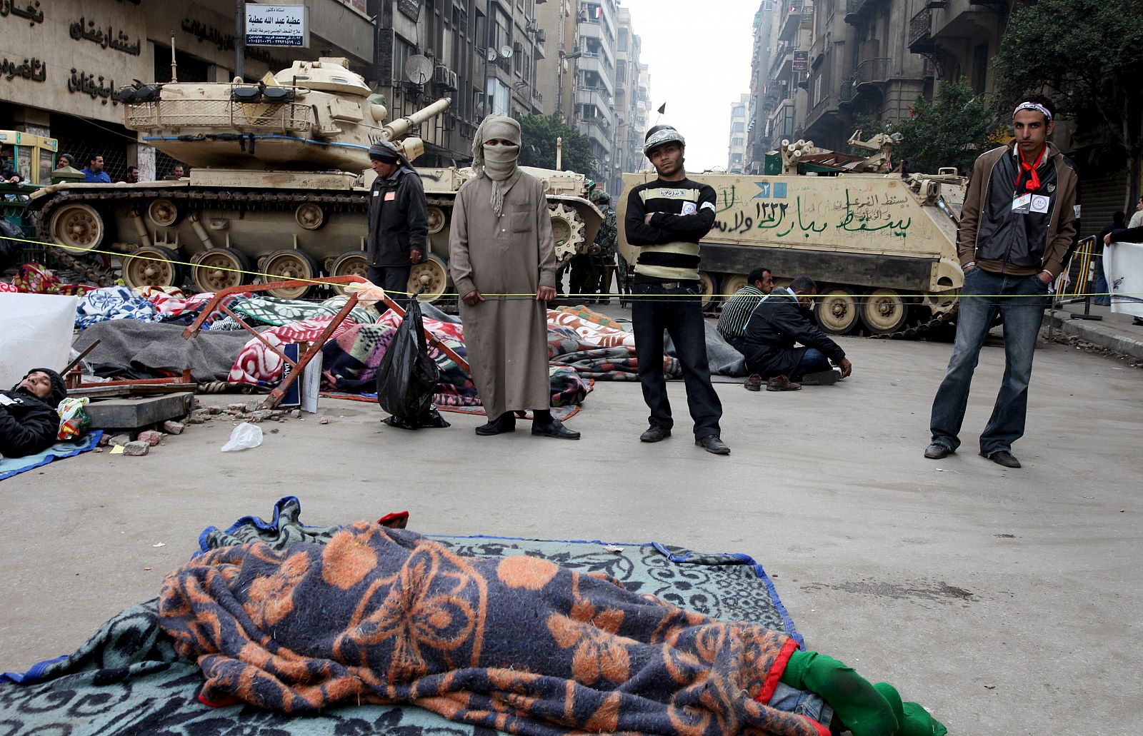 Manifestantes opositores al Gobierno permanecen en un puesto de control montado por civiles cerca de un tanque del ejército mientras otras personas duermen en una calle que conduce a la plaza Tahrir en El Cairo