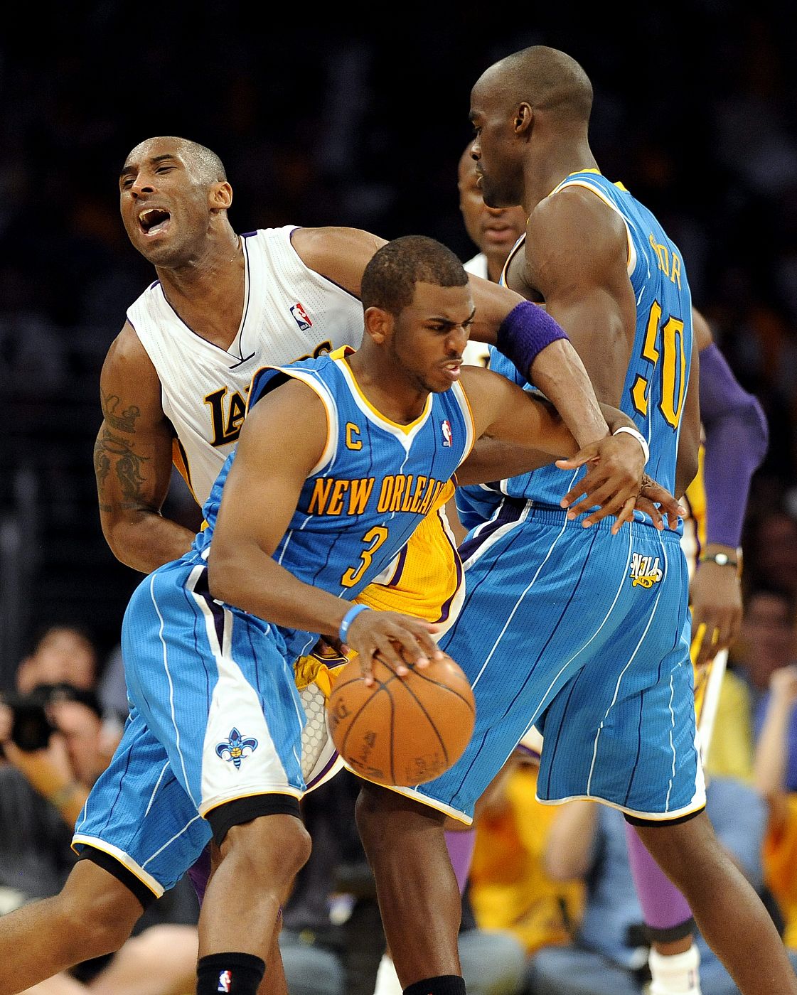 El jugador de Hornets Emeka Okafor (d) bloquea la marca de Kobe Bryant (i), de Lakers, a Chris Paul (c).