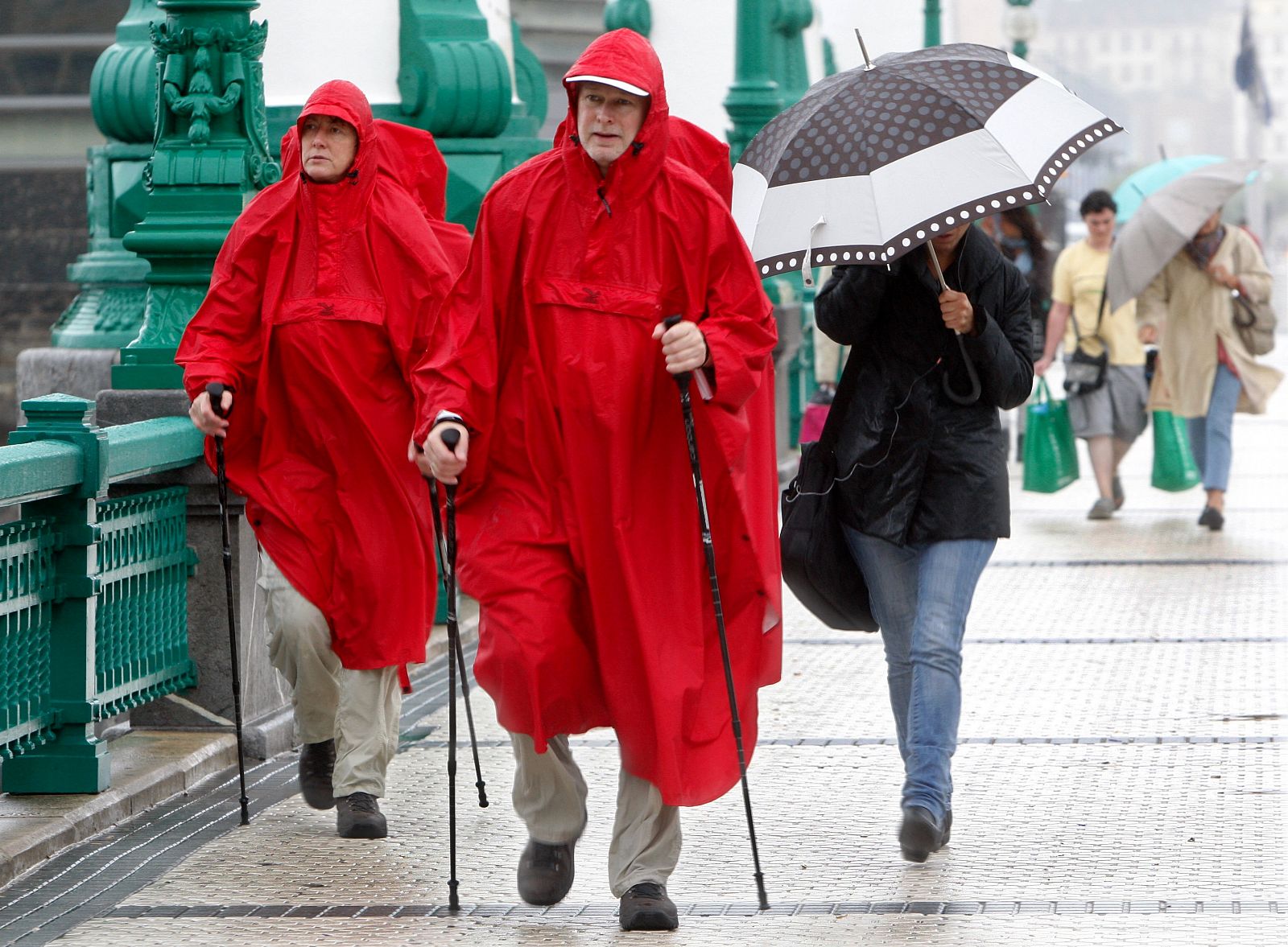 Una pareja de turistas cruza pasea por San Sebastián ataviados con chubasqueros para protegerse de la lluvia