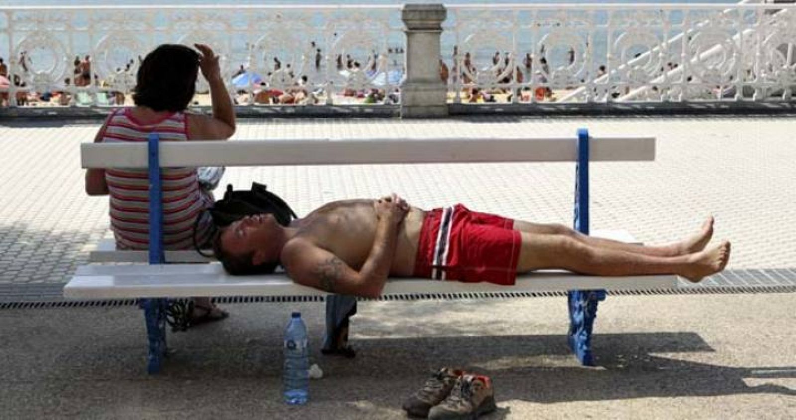 Dos personas descansan a la sombra en el paseo de la playa de La Concha de San Sebastián.