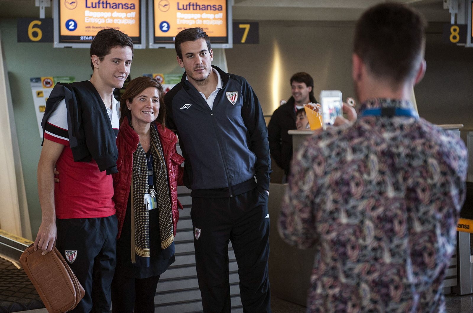 Los jugadores del Athletic de Bilbao Asier Goti (d) y Aymeric Laporte (i) se hacen una foto con una admiradora en el aeropuerto bilbaíno