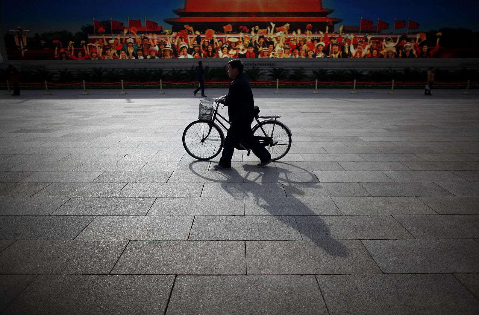 Un hombre pasa con su bicicleta frente a un cartel de propaganda en la Plaza de Tiananmen de Pekín