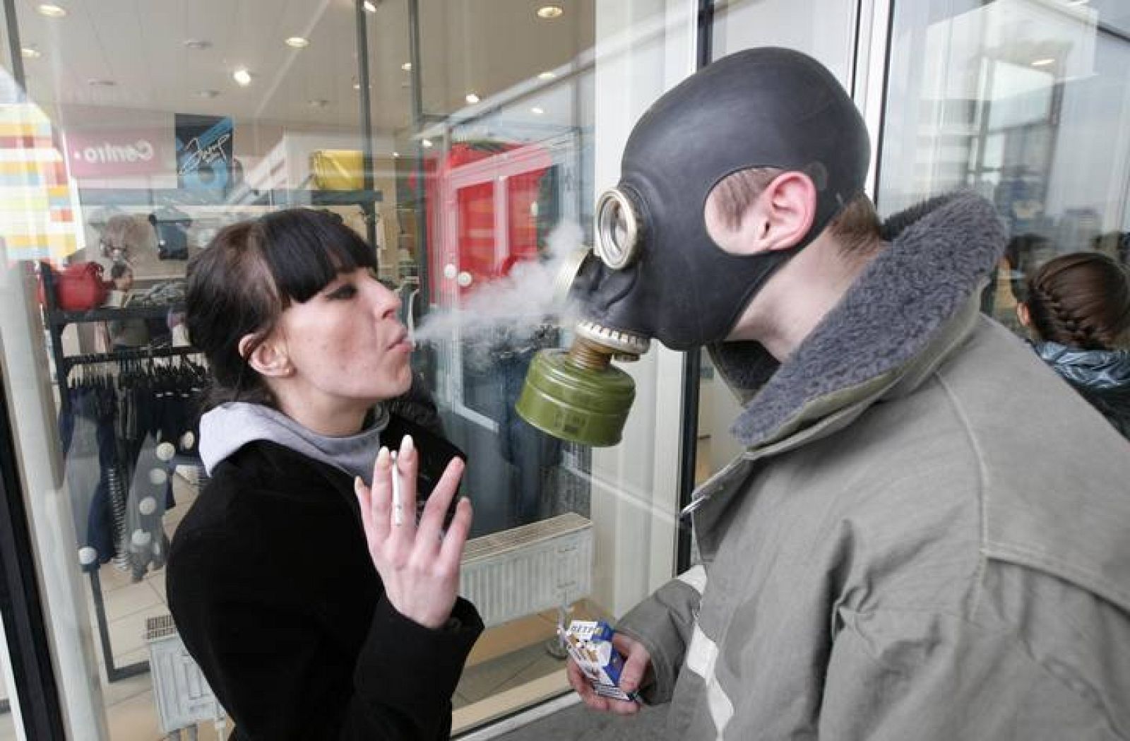 Una mujer lanza humo sobre un activista que lleva una máscara antigás e nun protesta anti tabaco en Rusia. 