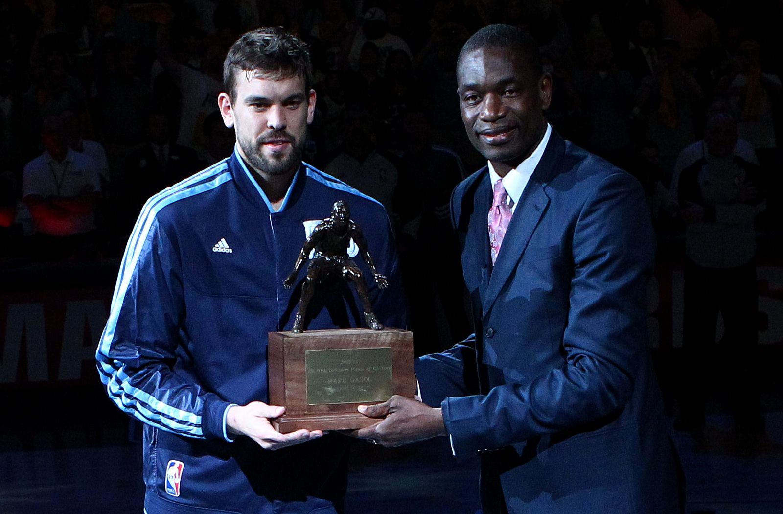 Marc Gasol (i), de los Grizzlies, recibe el trofeo Jugador Defensivo del Año de manos del exjugador de los Rockets, Dikembe Mutombo