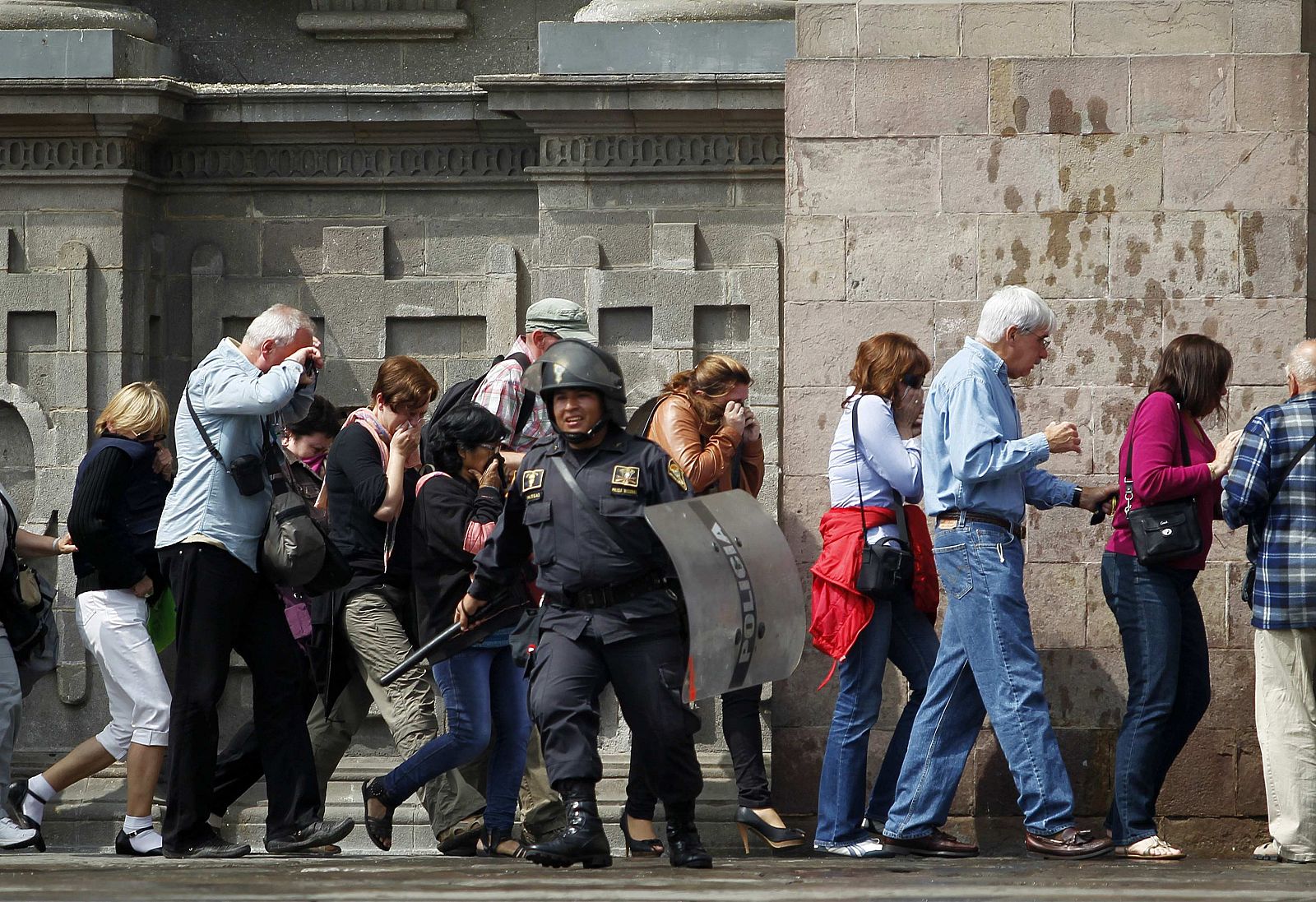 Turistas atrapados entre manifestantes y policías se protegen de los gases lacrimógenos y chorros de agua en la Plaza de Armas de Lima.