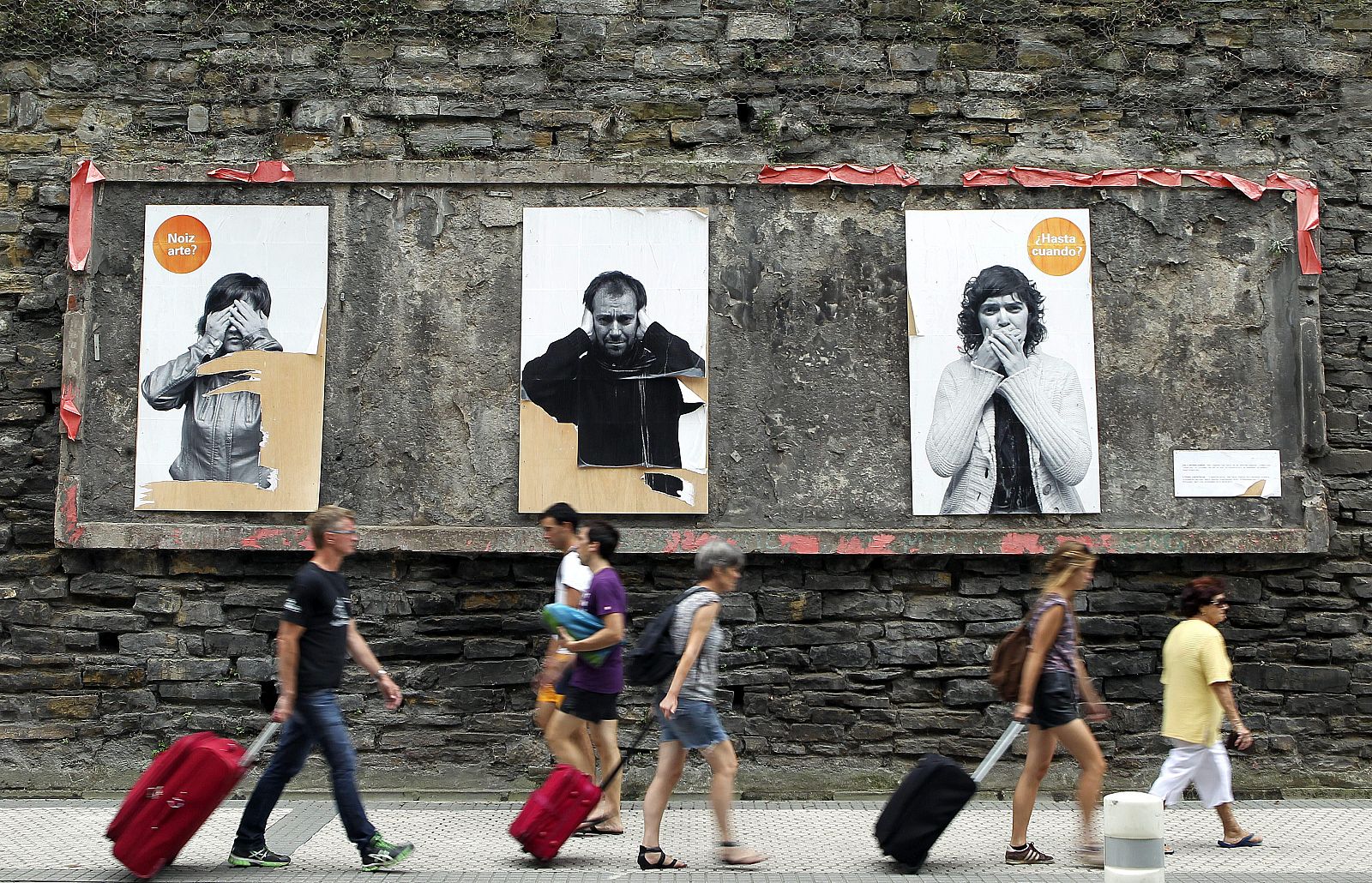 Varios turistas pasan junto a un panel publicitario en San Sebastián, donde el turismo extranjero ha compensado la caída de visitantes nacionales