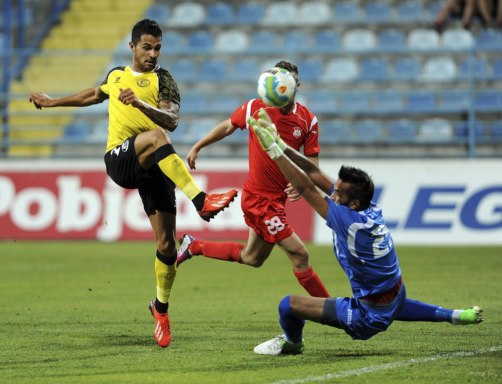 El jugador del Sevilla Víctor Machín trata de superar al portero Miroslav Vujadinovic en presencia de Ivan Novovic, ambos del Mladost Podgorica.