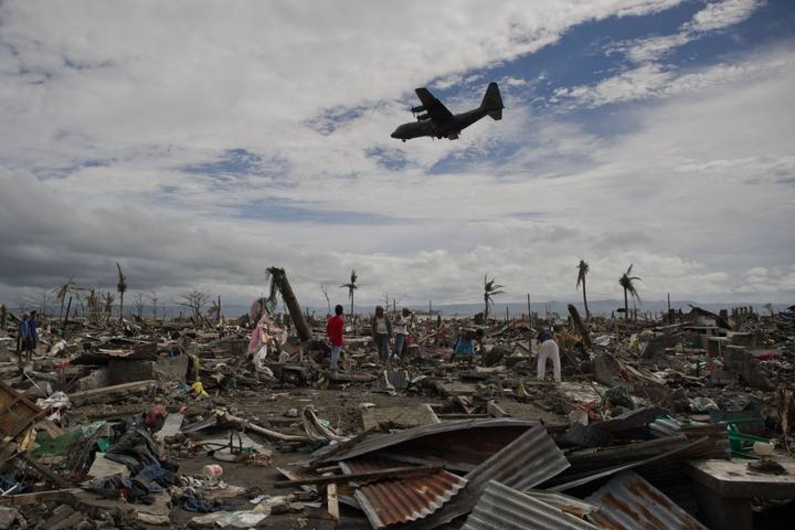 Damnificados del tifón Haiyan, entre las ruinas de sus casas mientras un avión con ayuda se dirige al aeropuerto de Tacloban