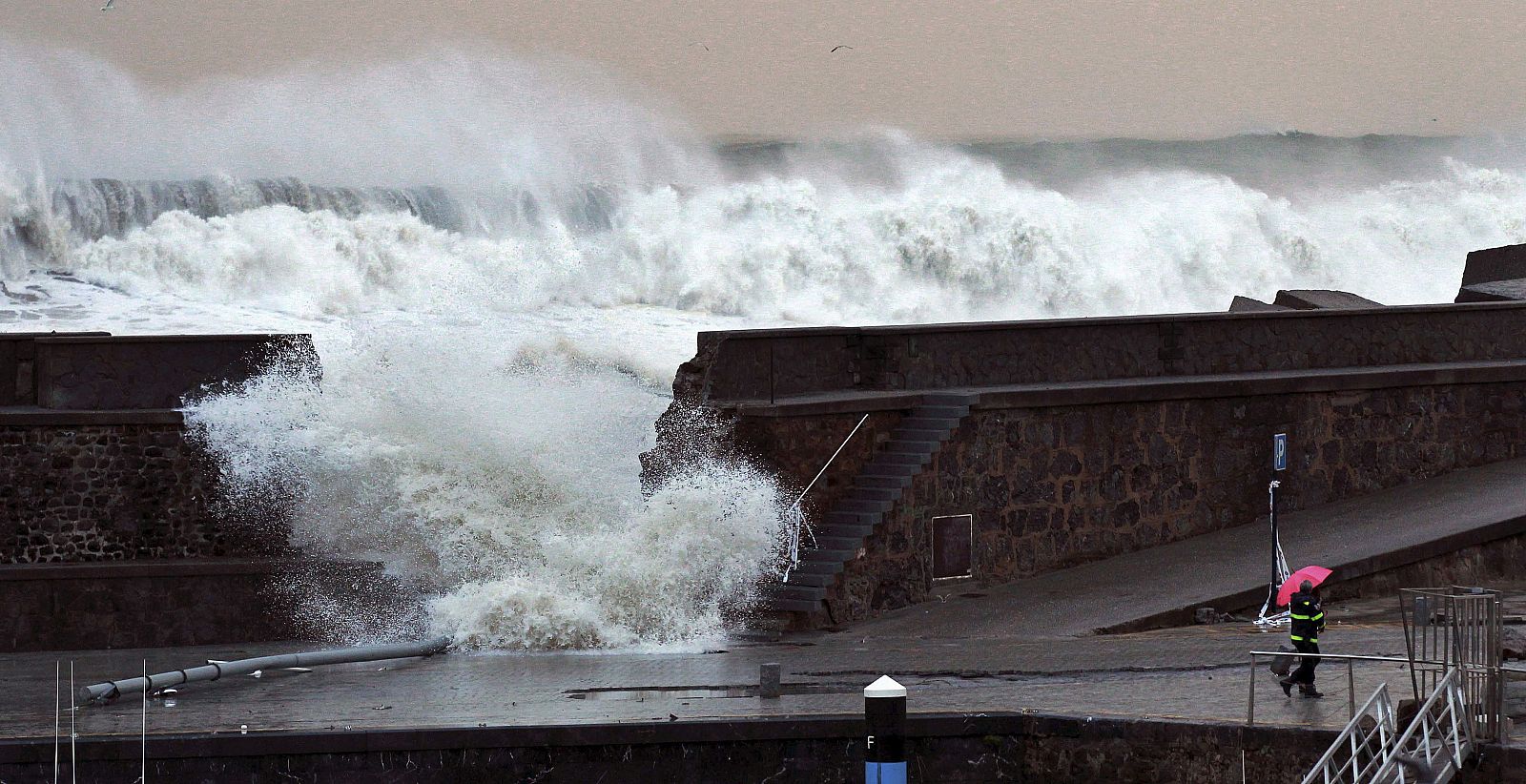 Dos personas caminan ante la brecha originada en el rompeolas del puerto de Bermeo.