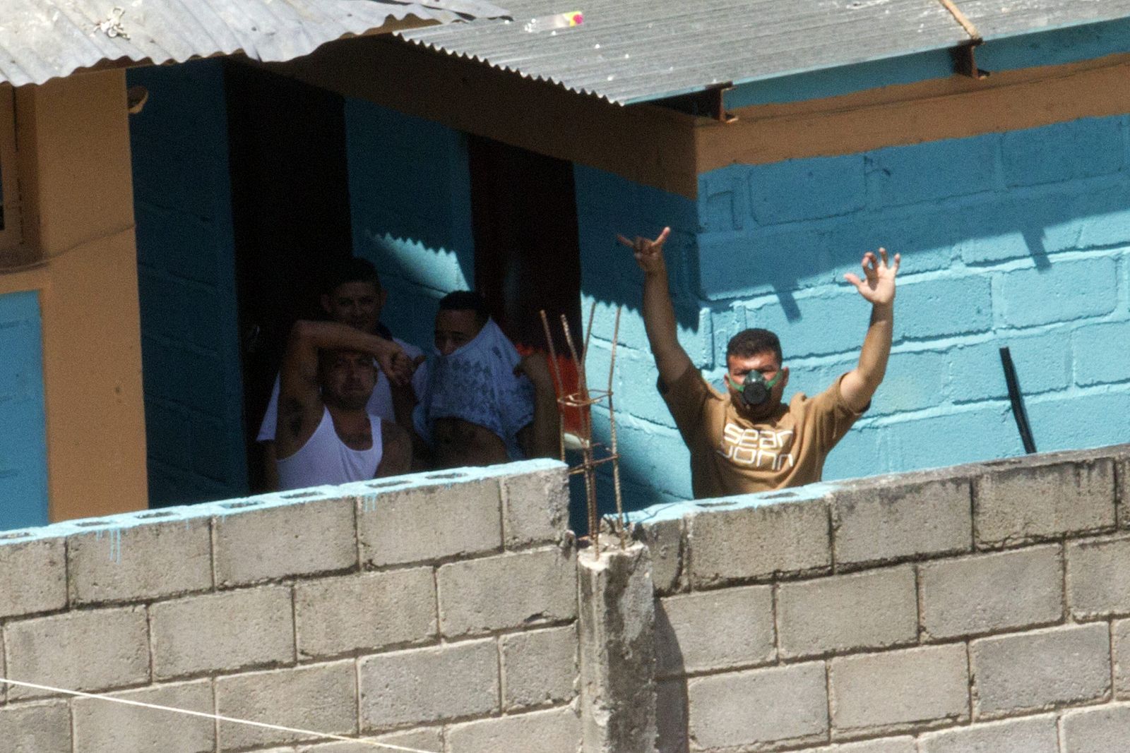 Reclusos hacen señas junto al muro de una cárcel de Tegucigalpa (Honduras).