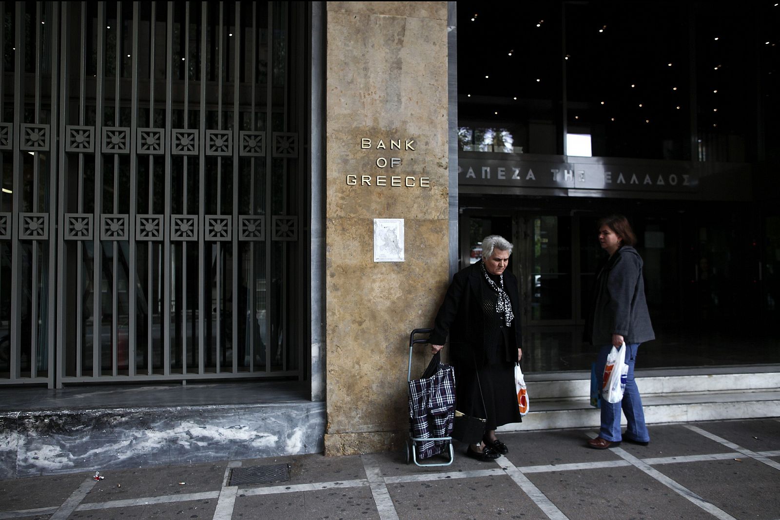 Dos mujeres con bolsas de compra conversan frente a la sede del Banco de Grecia en Atenas