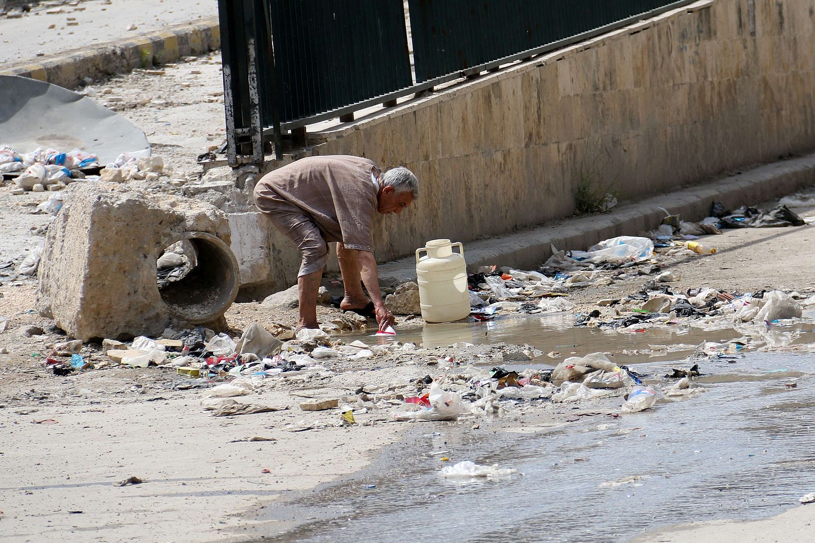 Un hombre recoge agua de un charco en la carretera en la ciudad de Aleppo