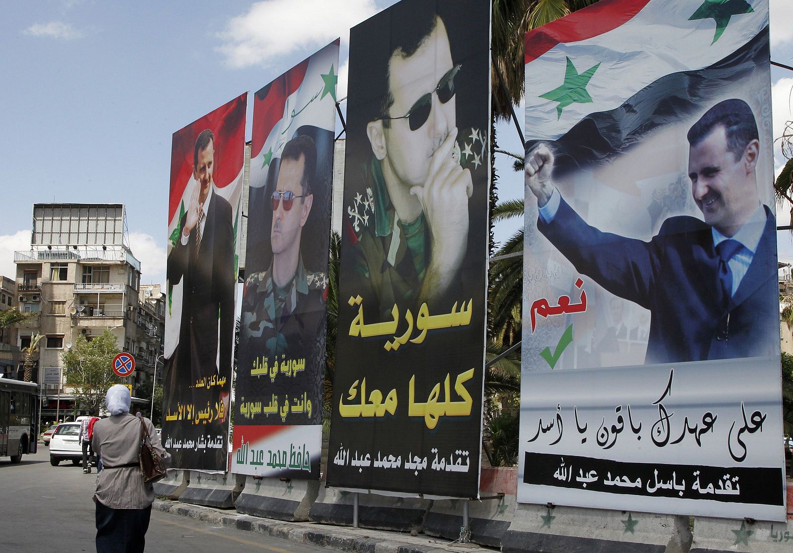 Una mujer pasa por delante de carteles propagandísticos de Bachar Al Asad en Damasco