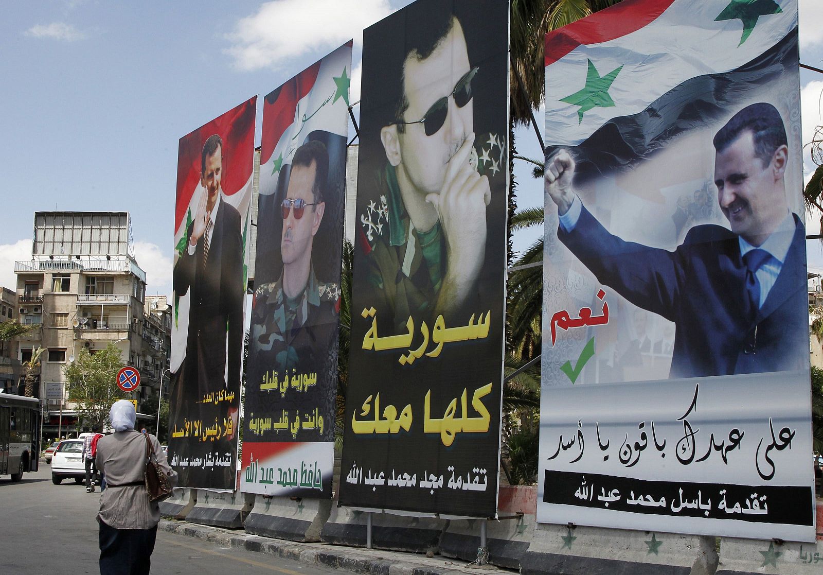 A woman walks past election posters of Syria's President Bashar al-Assad along a street in Damascus