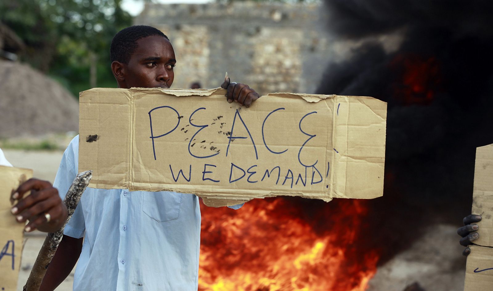 Un joven en la localidad de Mpeketoni muestra un cartel en el que pide "paz" delante de una barricada en protesta por la inseguridad en Kenia.