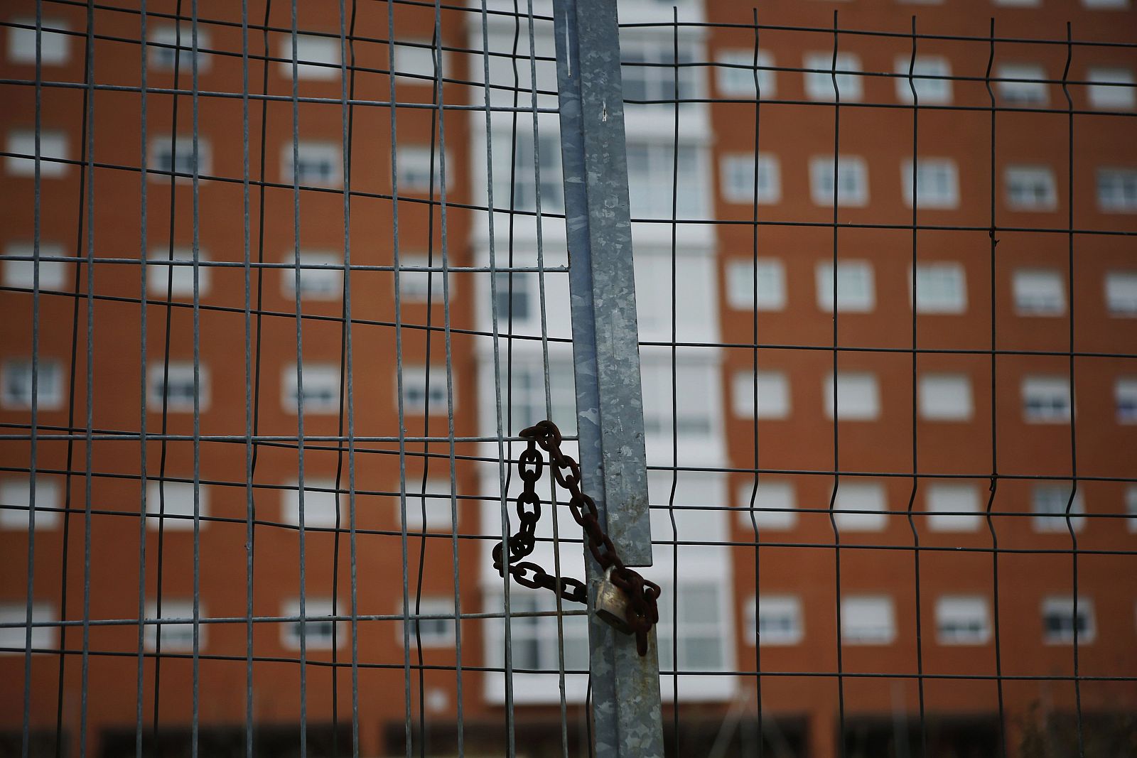 Un candado en una valla que rodea varias viviendas en Madrid