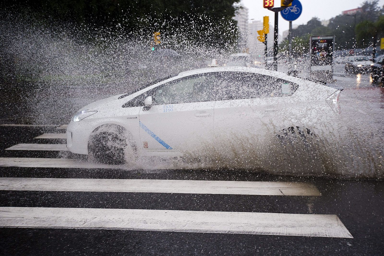 Un taxi pasa por un charco en un paso de cebra en Málaga