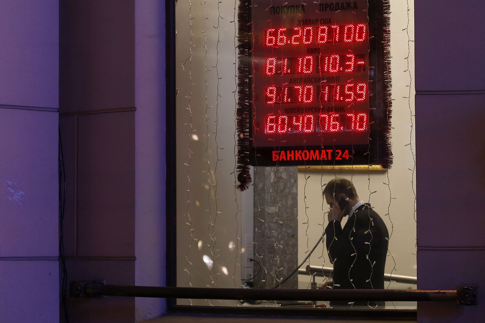 Silueta de un hombre a través de una ventana, junto a un cartel con los tipos de cambio en Moscú