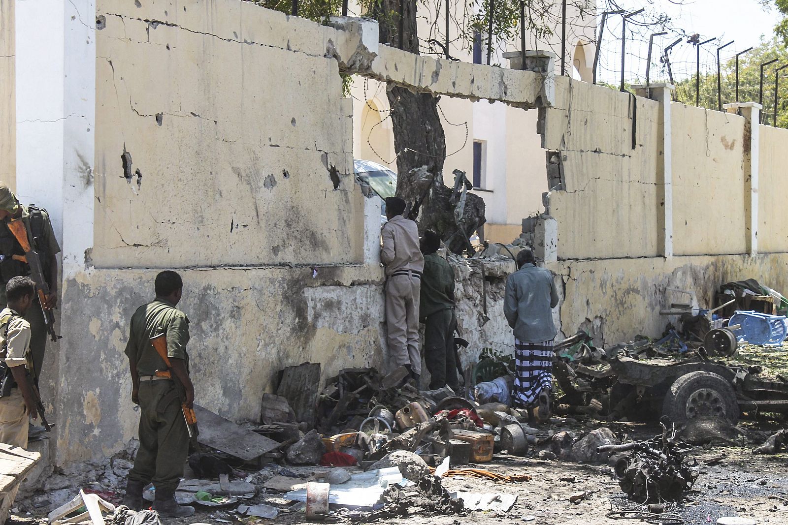 Miembros de las Fuerzas de Seguridad somalíes se asoman al interior junto al muro de un edificio gubernamental atacado por yihadistas en Mogdiscio (Somalia)