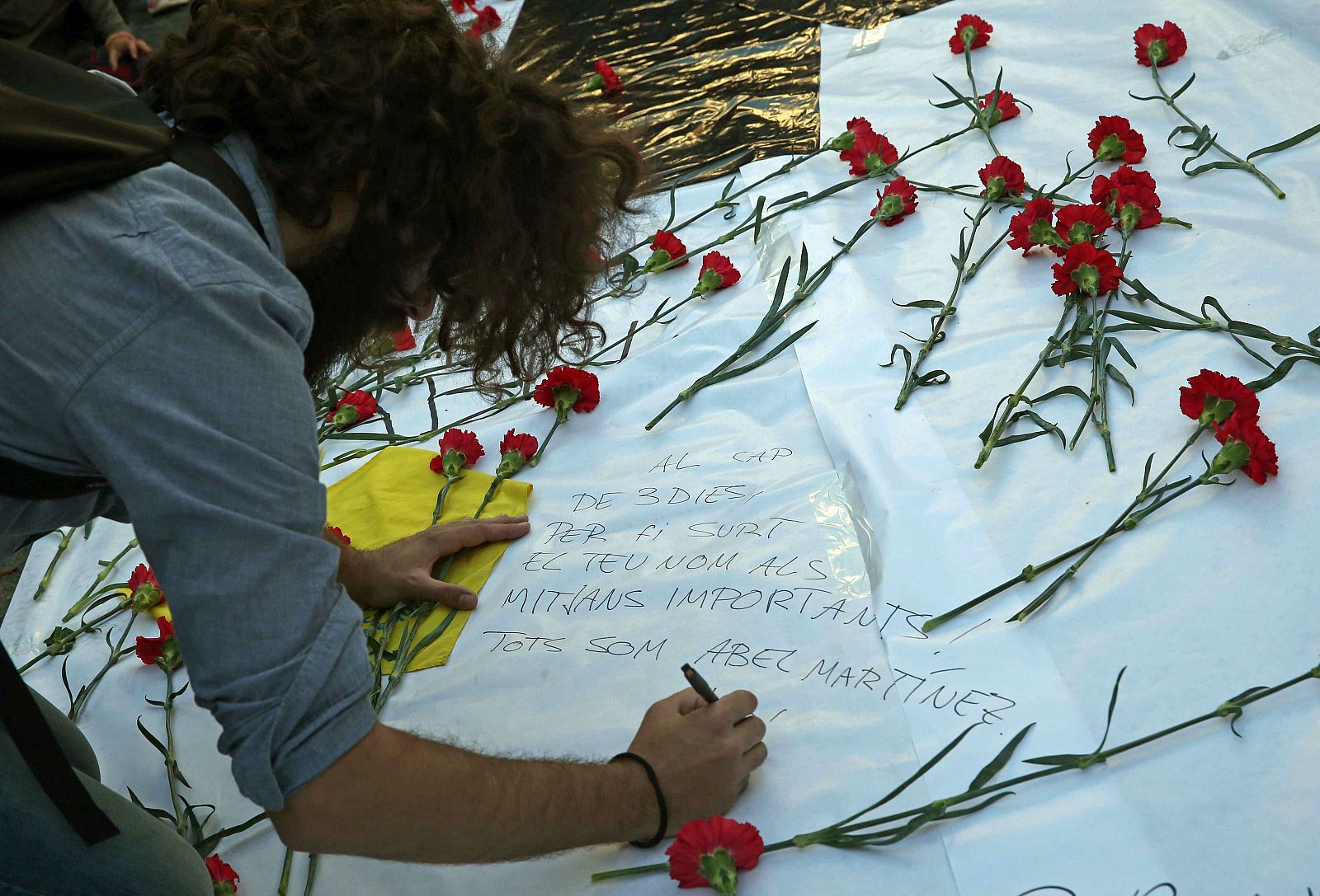 Un hombre escribe en una pancarta de homenaje a Abel Martínez, el profesor asesinado por un alumno de 13 años del instituto Joan Fuster de Barcelona.