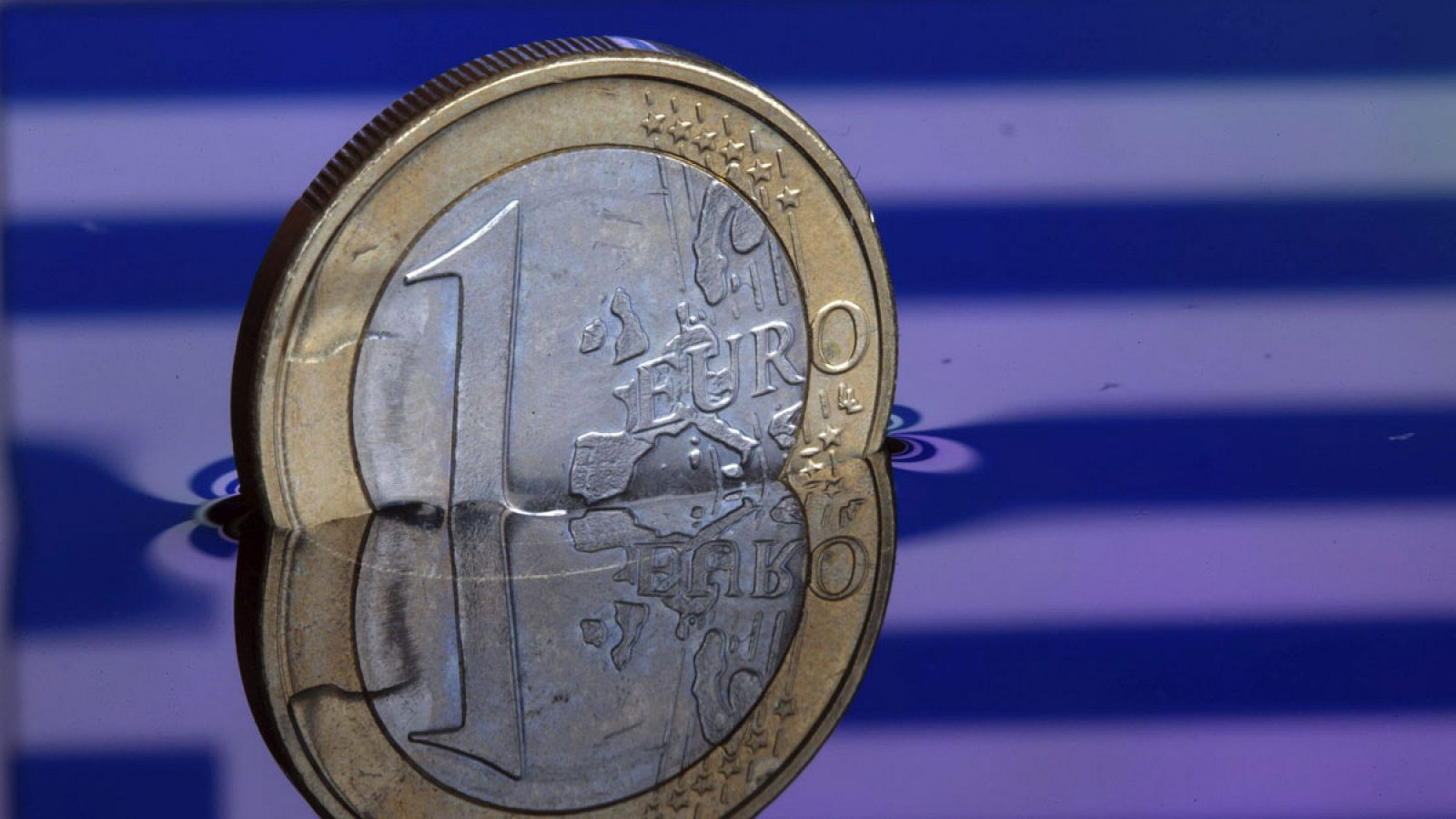 Una moneda de euro con la bandera de Grecia de fondo