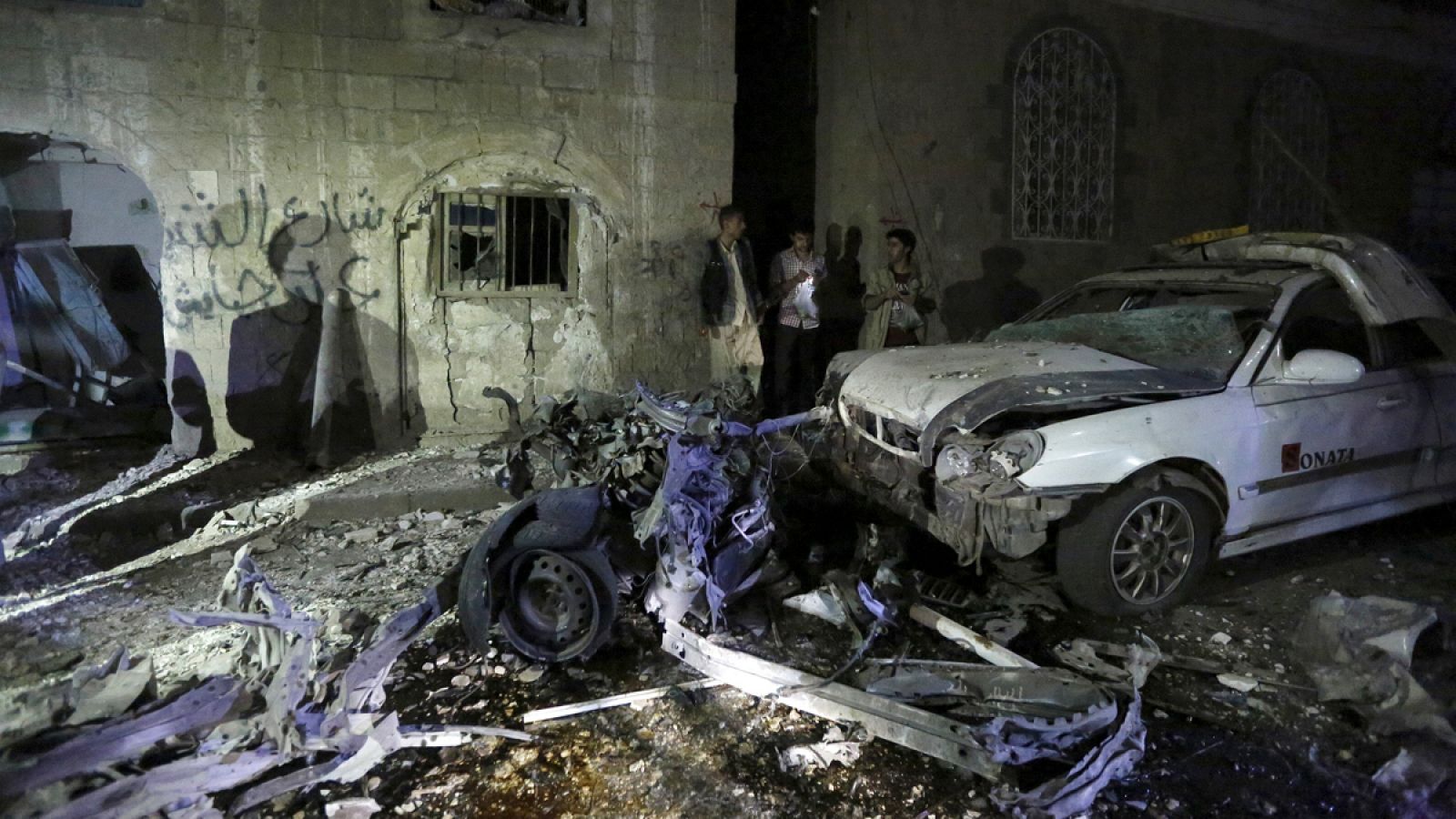 Un grupo de hombres observa los restos de un coche calcinado tras un ataque con coche bomba en Saná, la capital de Yemen, perpetrado por el EI.