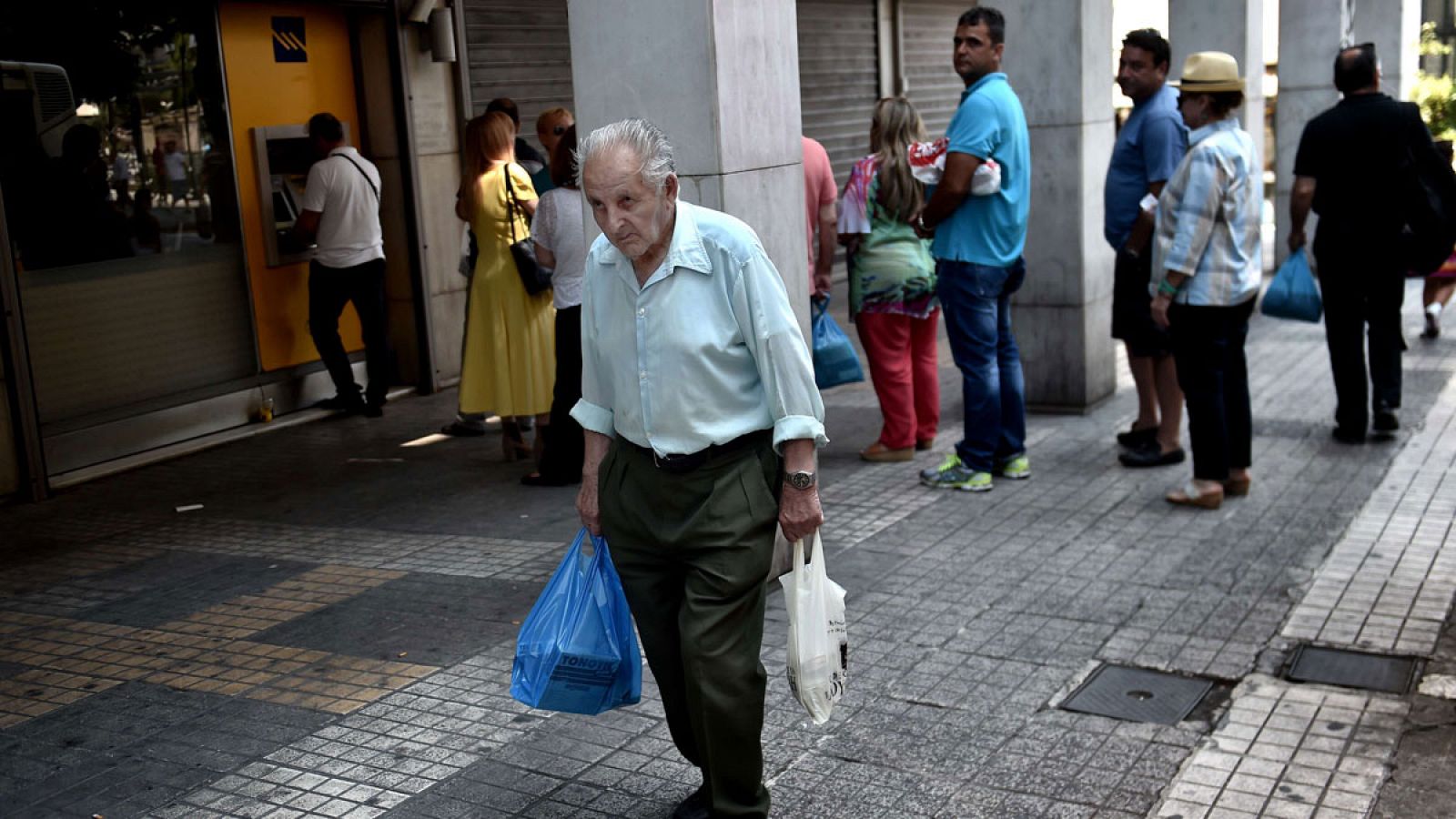 Un anciano pasa junto a una cola de personas ante un cajero en el centro de Atenas