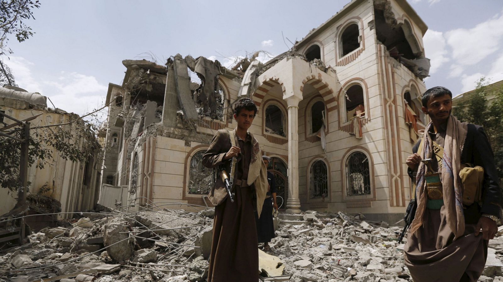 Dos hombres armados caminan a través de las ruinas de la casa de un comandante fiel a los hutíes tras dos bombardeos de la coalición árabe liderada por Arabia Saudí en Saná, Yemen.