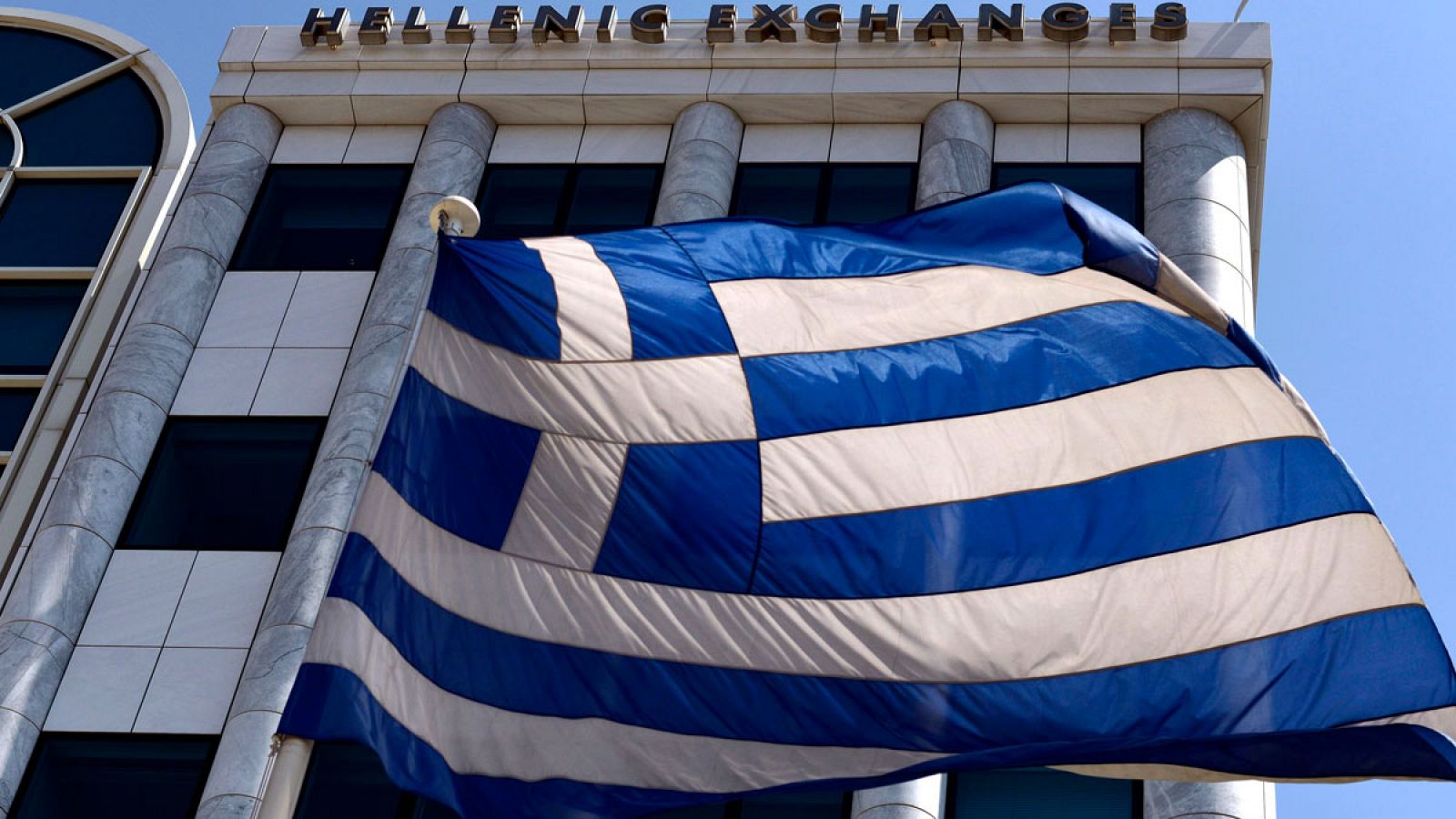 Imagen de una bandera griega que ondea delante de la Bolsa de Atenas
