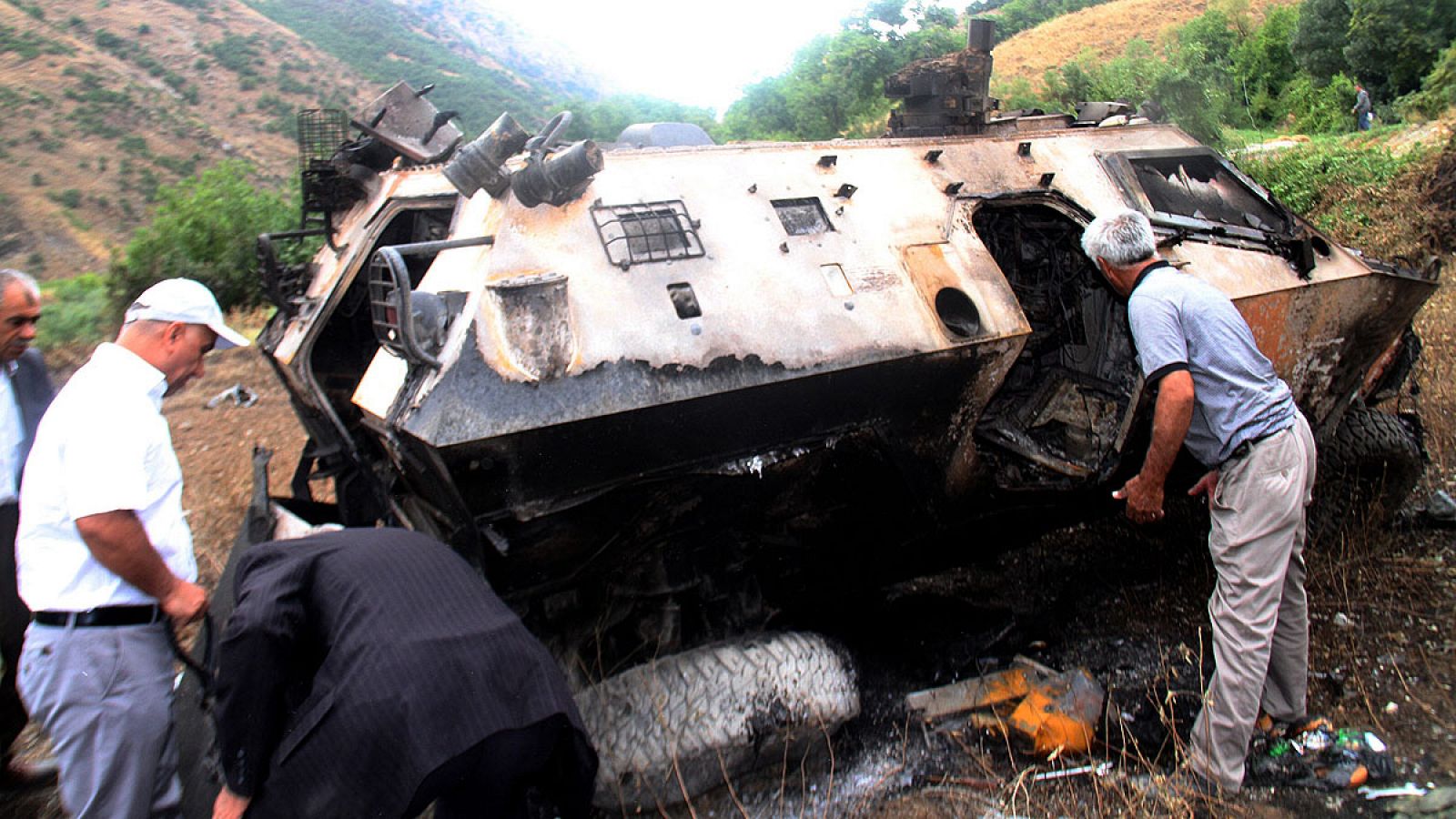 Lugareños observan los restos de un vehículo blindado turco destruido en el ataque del PKK en Daglica, sureste de Turquía