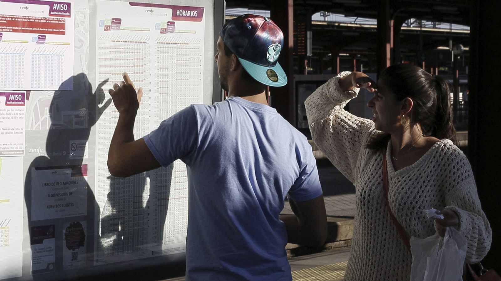 Dos pasajeros comprueban en un panel informativo los horarios de los trenes de Renfe en un andén de la estación de Chamartín, Madrid