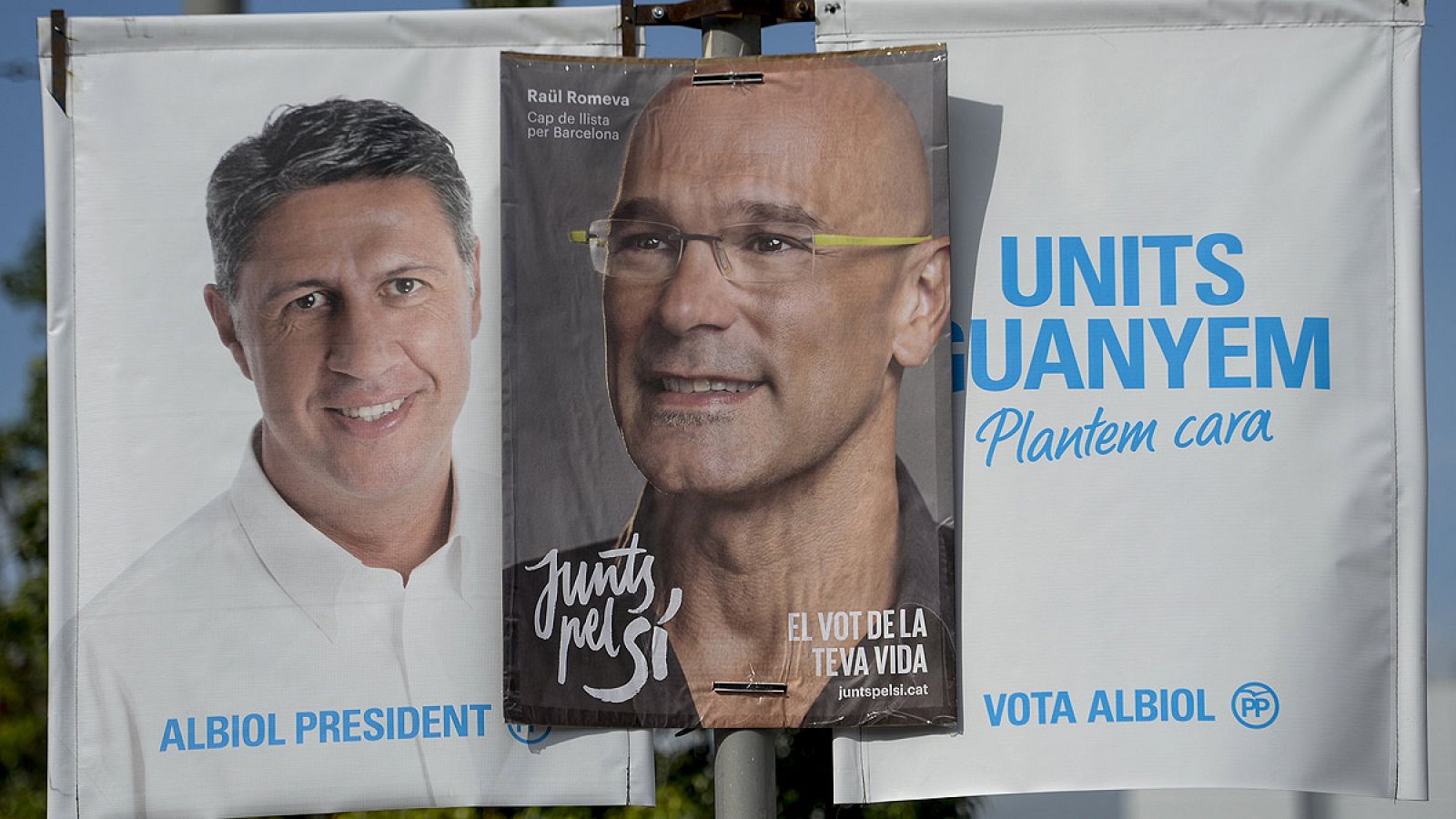 Dos posters electorales de los candidatos del PP y Junts pel Sí en las elecciones catalanas comparten espacio en una misma farola.