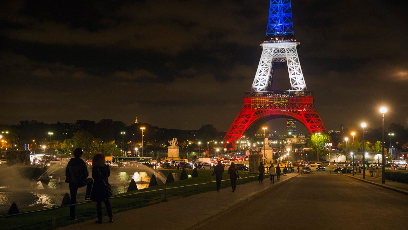 Varias personas observan la torre Eiffel iluminada con los colores de la bandera nacional francesa en París