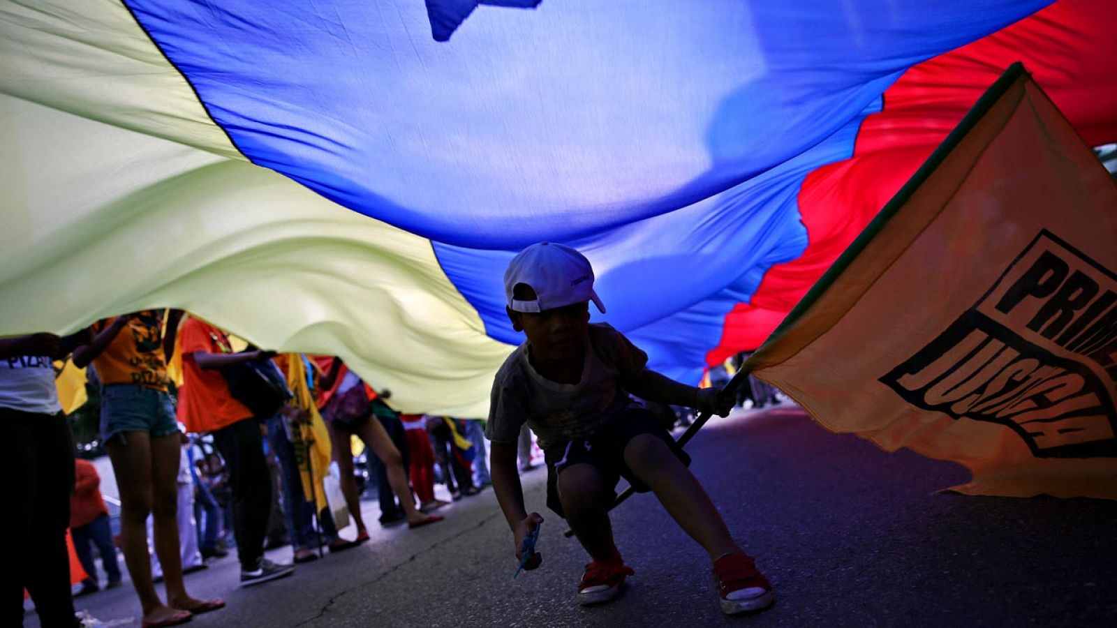 Un niño pasa bajo una enorme bandera de Venezuela durante un mitin electoral