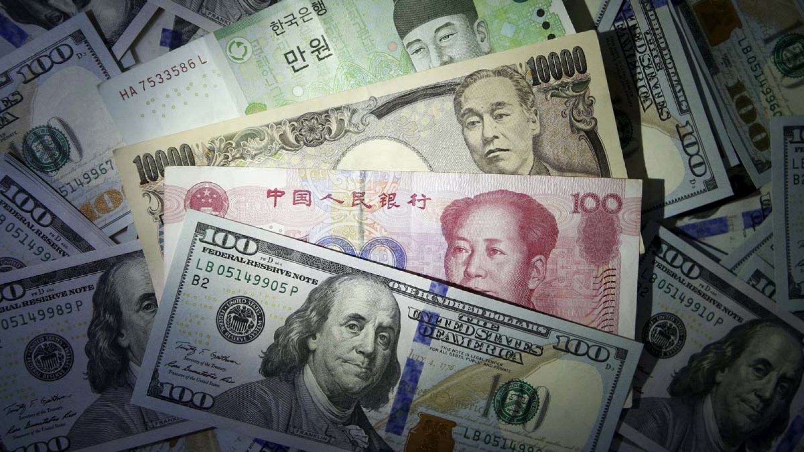 Un billete de 100 dólares estadounidenses junto a otros de won surcoreano, yen japonés y yuan chino