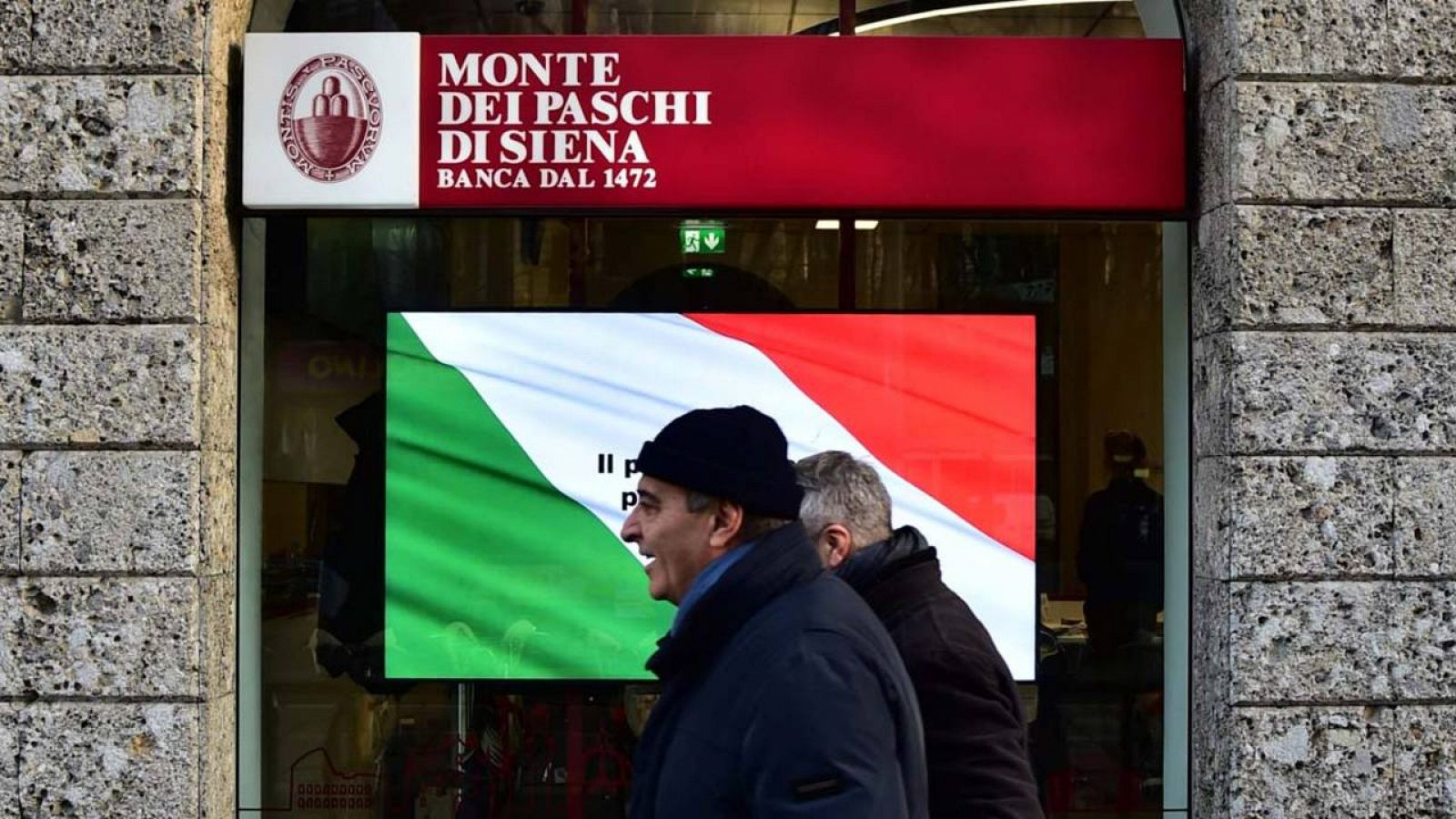 Varios transeúntes pasan delante de una oficina en Milán del Monte Dei Paschi di Siena