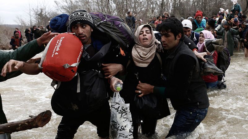 Grupo de refugiados tratando de un río en la frontera entre Grecia y Macedonia