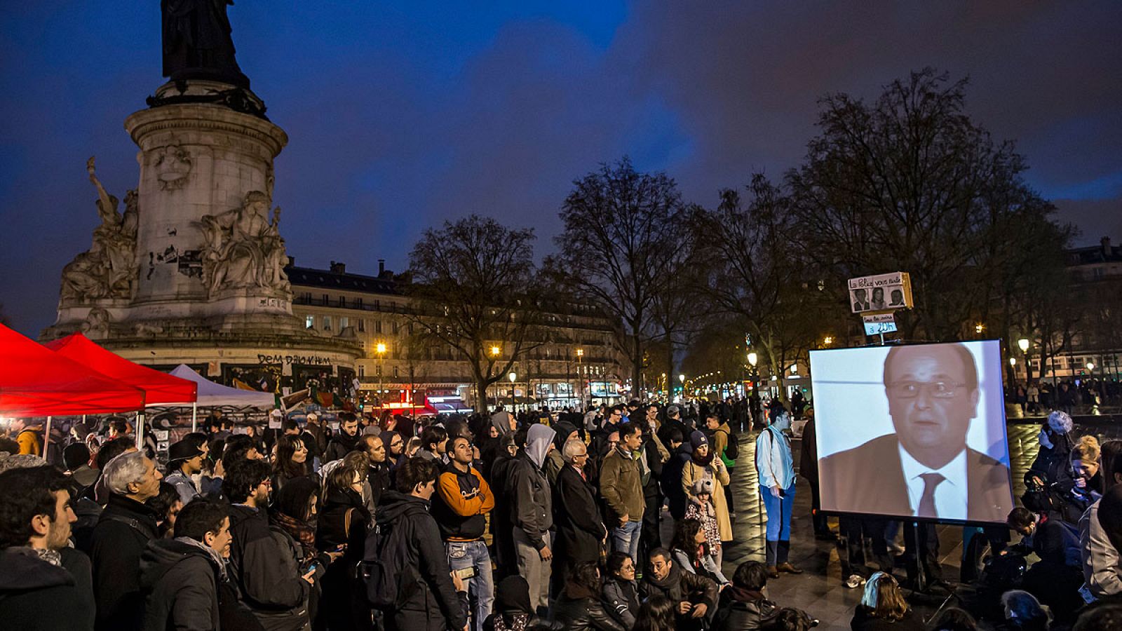 Integrantes del movimiento La Nuit Debout observan una intervención de Hollande desde la Plaza de la República