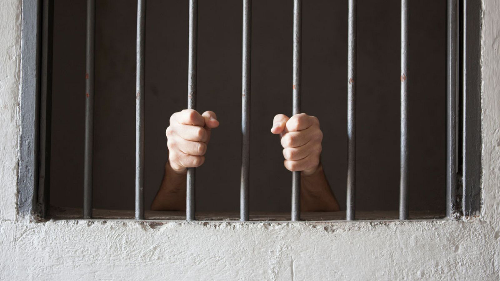 Manos agarrando los barrotes de una celda en una prisión