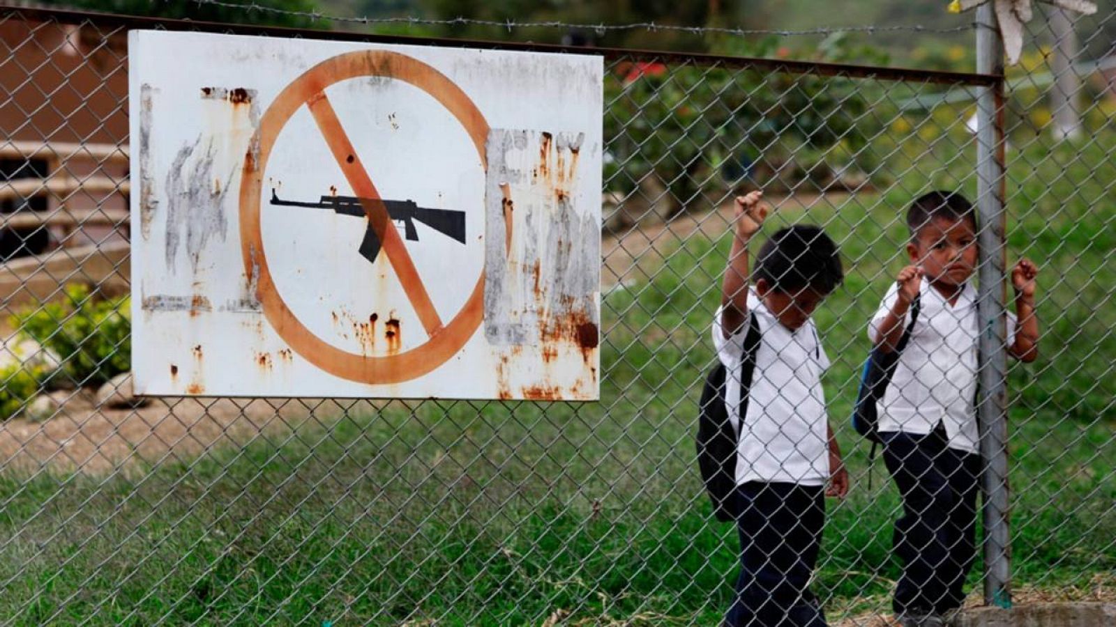 Dos niños en un colegio en Toribio (Colombia) junto a un cartel que indica la prohibición de llevar armas